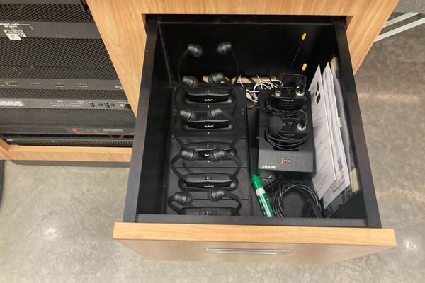 Pedestal - inside view of drawer showing two wireless mics in charging base and assistive listening devices in charger