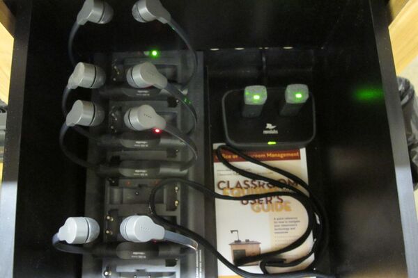 Pedestal - inside view of drawer showing two wireless mics in charging base and assistive listening devices in charger