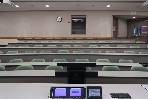 Back of room view of student tiered fixed-table and chair seating and double exit doors at right rear of room