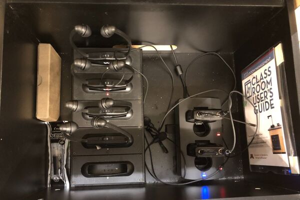 Pedestal - inside view of drawer showing two wireless mics in charging base and assistive listening devices in charger