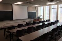  Front of room view with lectern on right in front of chalkboard and projection screen fully lowered