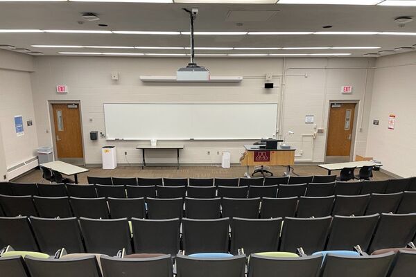 Front of room view with lectern on right in front of markerboard and exit doors to left and right