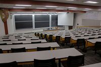 Front of room view with lectern center in front of chalkboards and projection screen lowered on the right