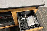 Pedestal - inside view of drawer showing two wireless mics in charging base and assistive listening devices in charger