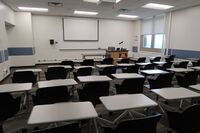 Front of room view with lectern on right in front of markerboard and projection screen lowered