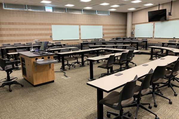 Back of room view of student tiered fixed-table and chair seating, markerboards on back and side walls, monitor on back wall