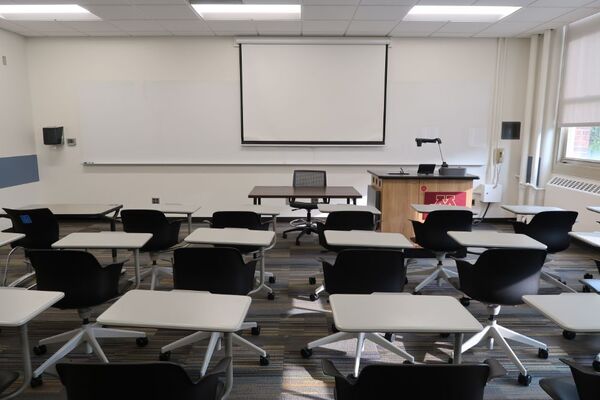 Front of room view with lectern on right in front of markerboard and projection screen lowered