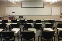 Front of room view with lectern on left in front of markerboard and projection screen partially raised