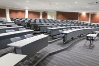 Back of room view of student tiered fixed table and chair seating and double exit door at right rear of room