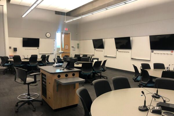 View of room shows student collaborative table and chair seating and exit door at rear of room