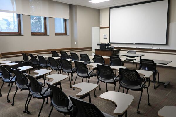 Front of room view with lectern on left in front of markerboard and projection screen lowered