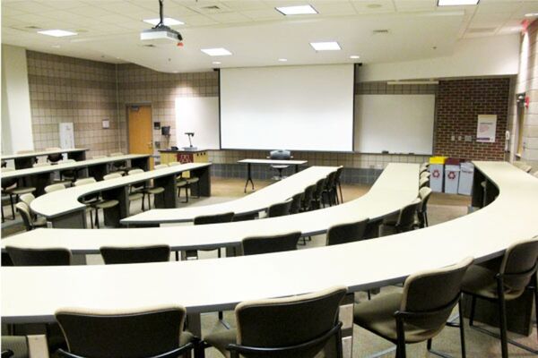 Front of room view with lectern on left in front of markerboard and projection screen lowered