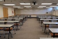 Back of room view of student table and chair seating and exit door at left rear of room