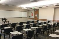 Front of room view with lectern on left in front of markerboard, exit door on right wall near front of room