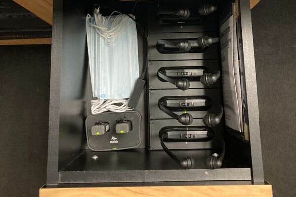 Pedestal - inside view of drawer showing two wireless mics in charging base and assistive listening devices in charger