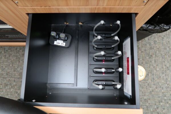 Pedestal - inside view of drawer showing two wireless mics in charging base and assistive listening devices in charger