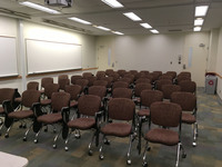 Photo of back of room from front of room with tablet armchairs on casters and doors at back.