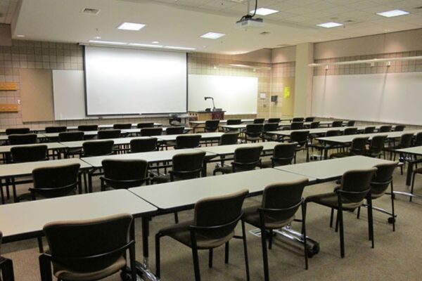 Front of room view with lectern on right in front of markerboard and projection screen lowered