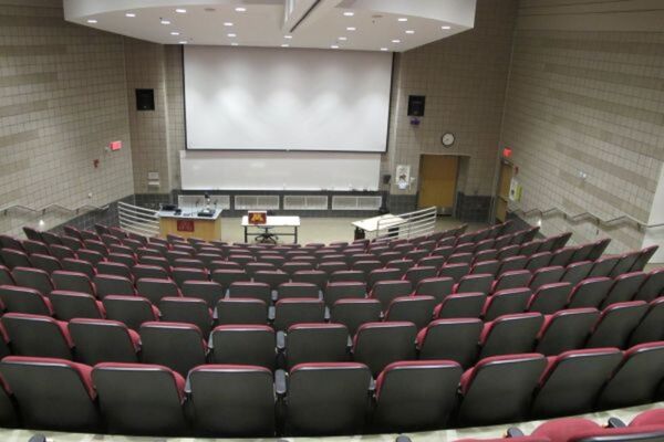 Front of room view with lectern on left in front of markerboard and projection screen lowered