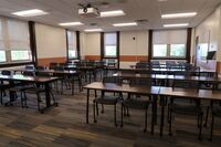 Back of room view of student table and chair seating and markerboard on right side wall of room