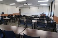 Front of room view with lectern on right in front of markerboard, projection screen partially raised, and exit at left front of room