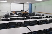 Front of room view with lectern on right in front of markerboard and projection screen lowered