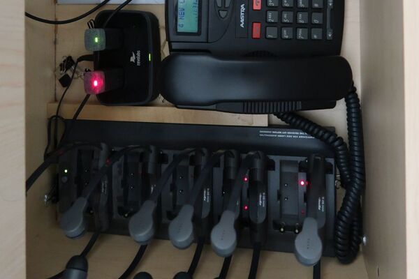 Pedestal - inside view of drawer showing two wireless mics in charging base, telephone, and assistive listening devices in charger