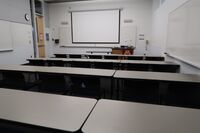 Front of room view with lectern on right in front of markerboard and projection screen lowered