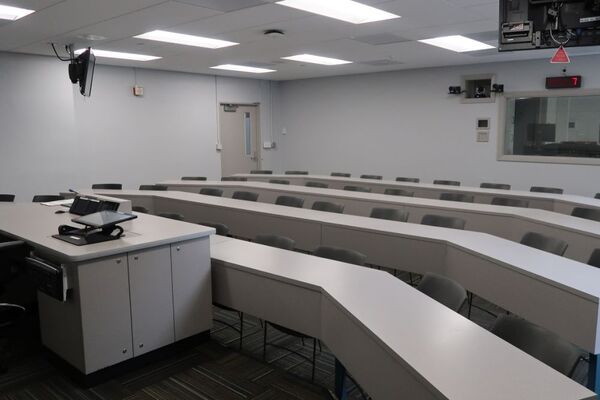 Back of room view of student tiered table and chair seating with exit door at left rear of room