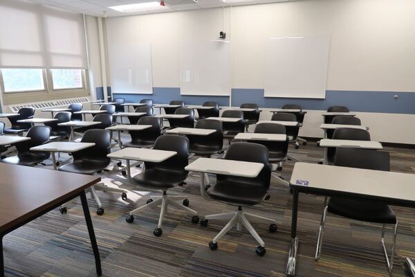 Back of room view of student tablet arm seating, markerboards, and camera on rear wall of room