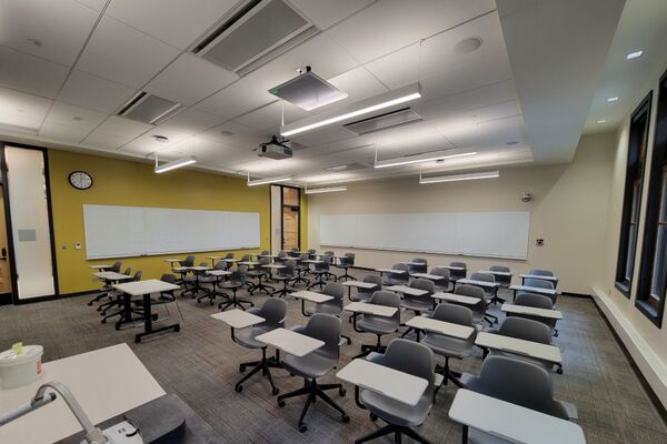 Back of room view of student tablet arm seating and markerboards on side and rear wall, exit door at left rear of room