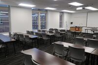 Front of room view with lectern on left in front of markerboard and projection screen lowered