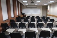 Front of room view with lectern on left in front of markerboard and projection screen partially raised