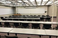 Front of room view with lectern on left in front of markerboard and projection screen partially raised