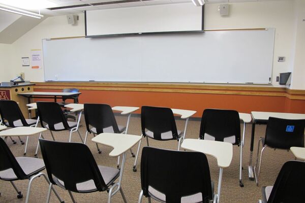 Front of room view with lectern on left in front of markerboard and projection screen partially raised