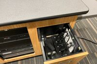 Pedestal - inside view of drawer showing two wireless mics in charging base and assistive listening devices in charger