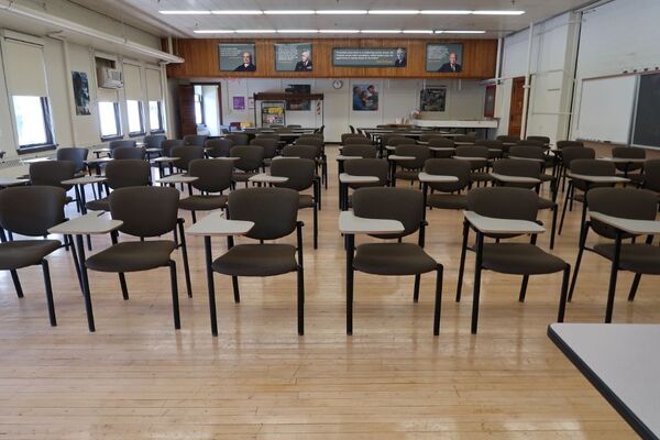 Back of room view of student tablet arm and table and chair seating, movable markerboard on right side of room, exit door located at left rear corner of the room