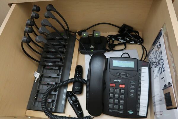 Pedestal - inside view of drawer showing two wireless mics in charging base, telephone, and assistive listening devices in charger