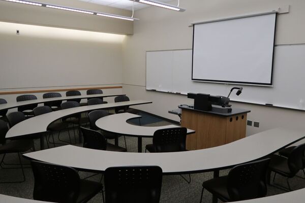 Front of room view with lectern on center in front of markerboard and projection screen lowered