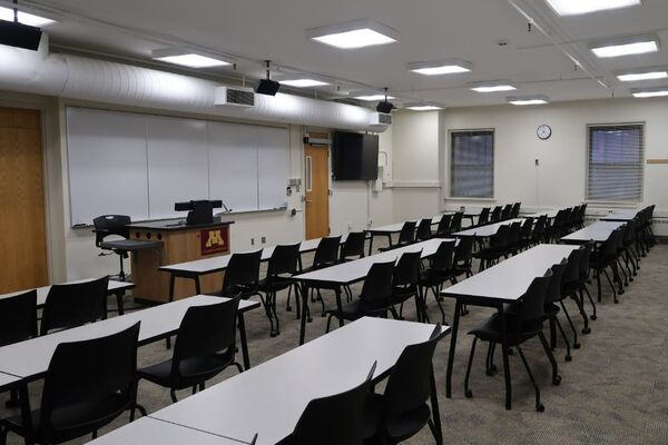 Front of room view with lectern on left in front of markerboard and exit door in front on the right