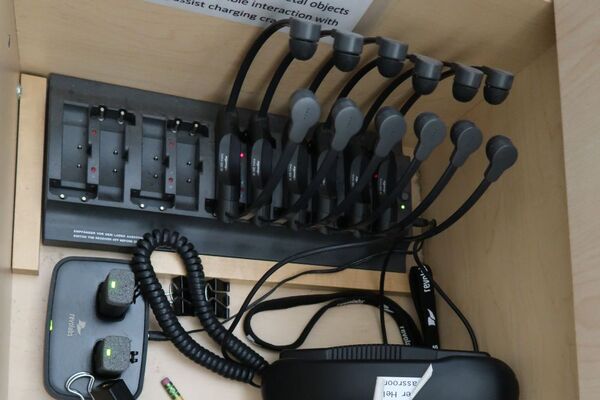 Pedestal - inside view of drawer showing two wireless mics in charging base and assistive listening devices in charger