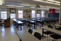 Back of room view of student table and chair seating and chalkboard on rear wall of room