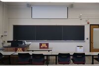 Front of room view with lectern on left side and projection screen partially lowered