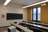 Rear of room view of student table and chair seating and chalkboard on left side of room