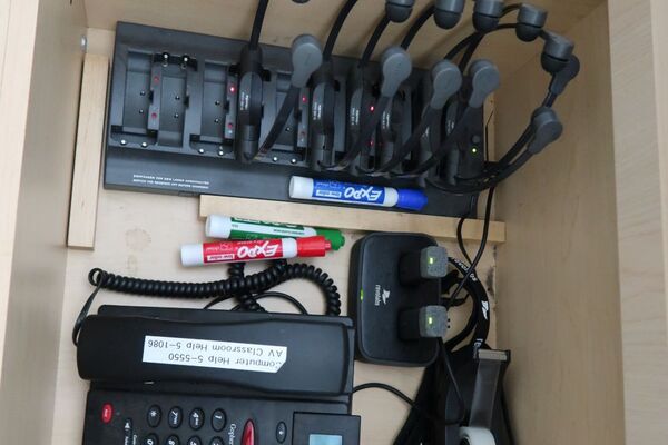 Pedestal - inside view of drawer showing two wireless mics in charging base, telephone, and assistive listening devices in charger