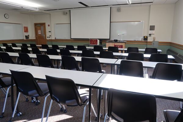 Front of room view with lectern on right in front of markerboard and projection screen lowered