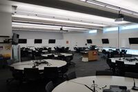 Room view of student active learning round table and chair seating, markerboards and student display monitors on all walls