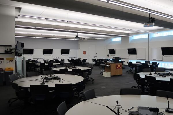 Room view of student active learning round table and chair seating, markerboards and student display monitors on all walls