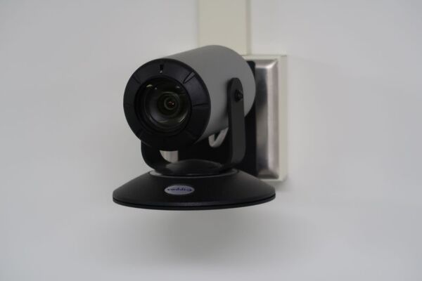 Camera mounted to a wall and instructor enabled adjustments to the lens to allow the instructor to be "seen" by the camera in more locations around the room