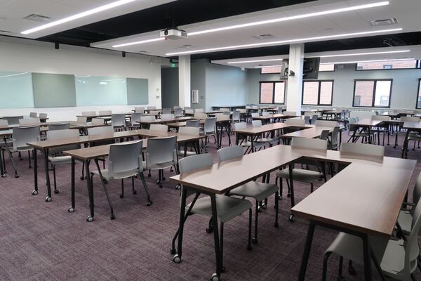 Back of room view of student tables and chairs, exit door, and vertical writing surfaces